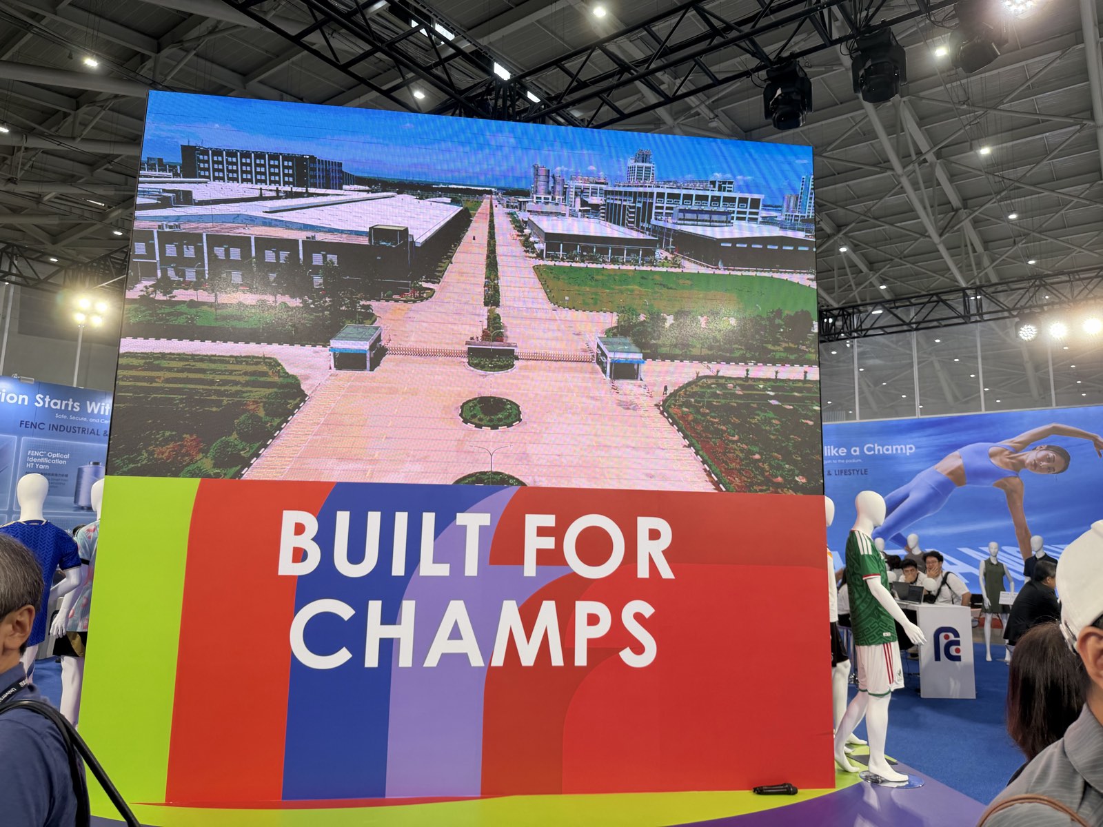 The central LED cube of the FENC booth reading BUILT FOR CHAMPS above an aerial view of a FENC plant