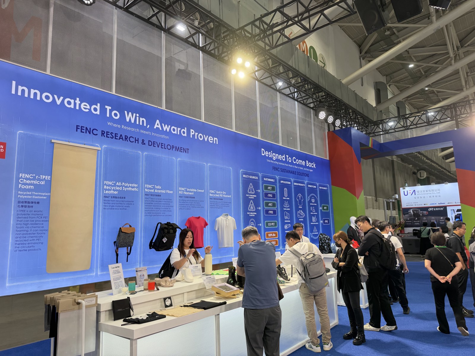 Blue R&D wall headed Innovated To Win, Award Proven with product panels, next to the Designed To Come Back recycling flow wall and a busy sample table